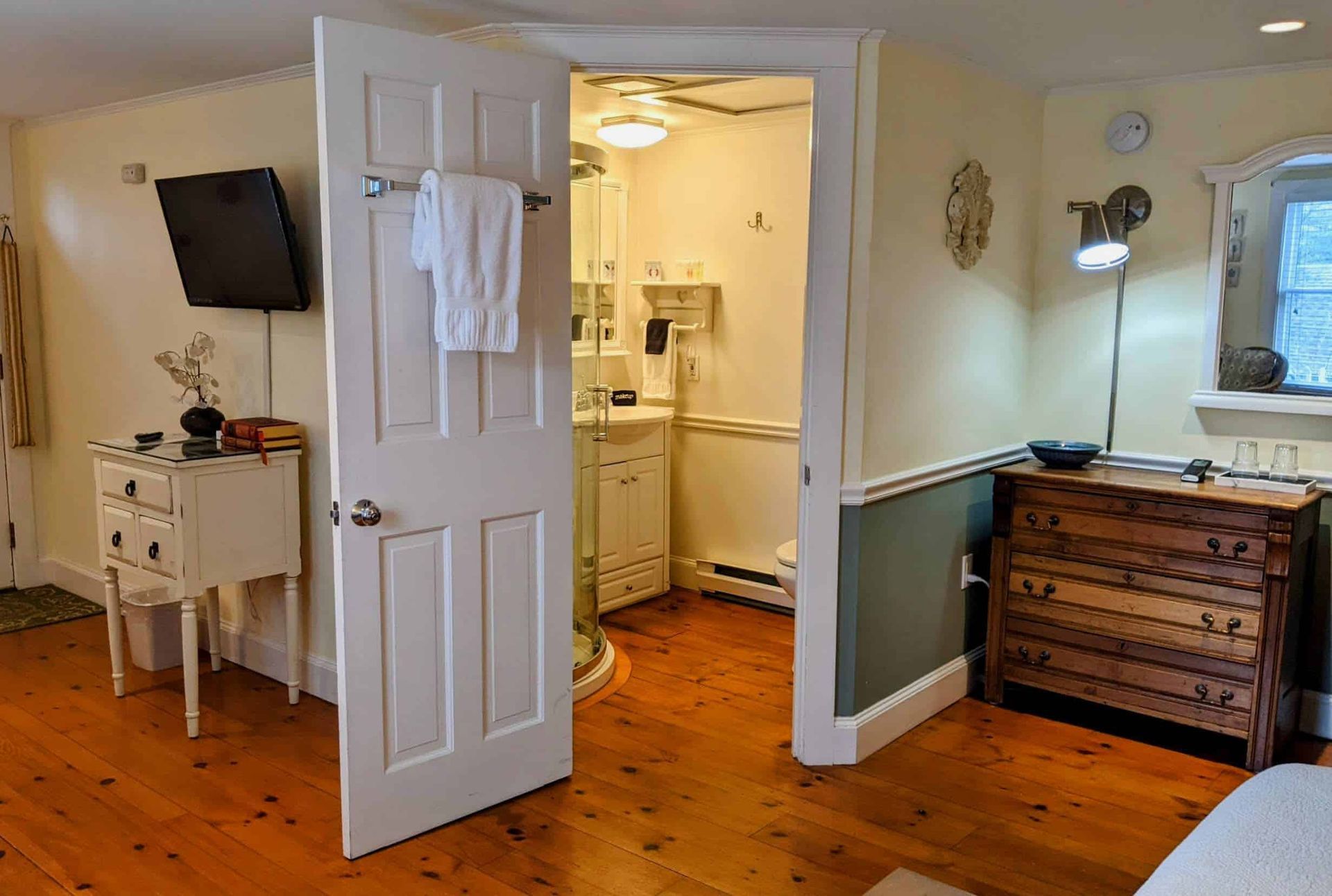 A bedroom with hardwood floors , a television , a dresser and a bathroom.