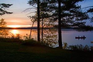 A sunset over a lake with trees in the foreground and a boat in the water.