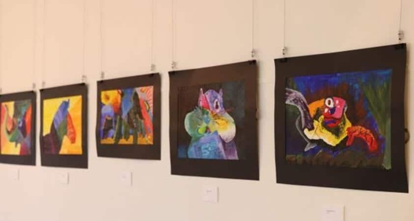 A row of colorful paintings are hanging on a wall.