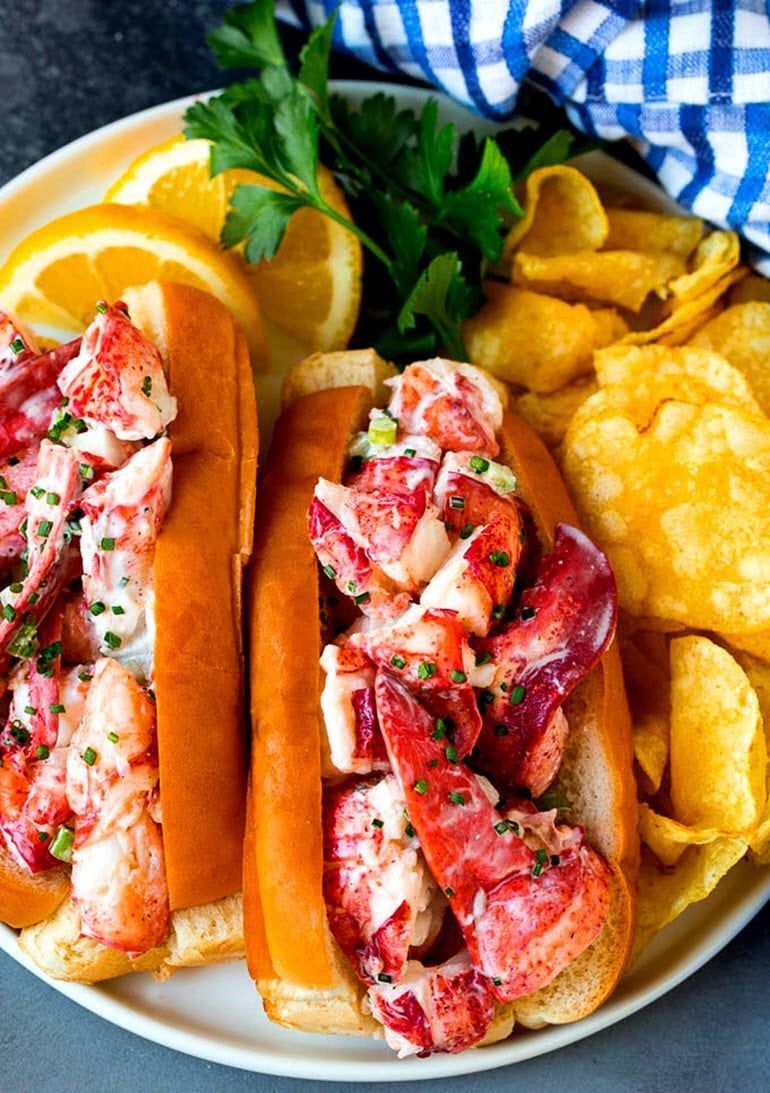 A white plate topped with two lobster rolls and potato chips.