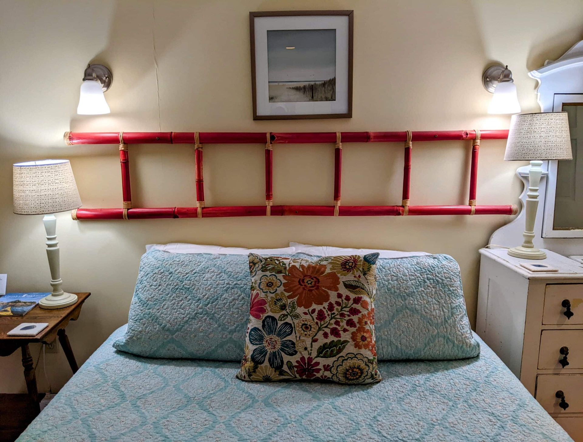 A bed with a ladder headboard and a picture on the wall above it.