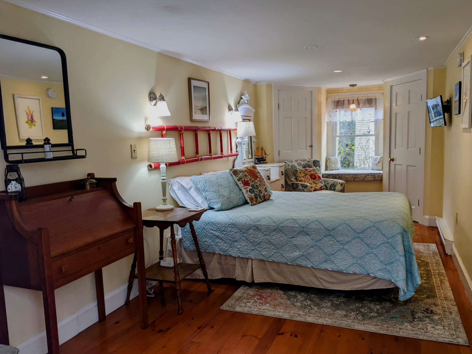 A bedroom with a bed , desk , mirror and window.
