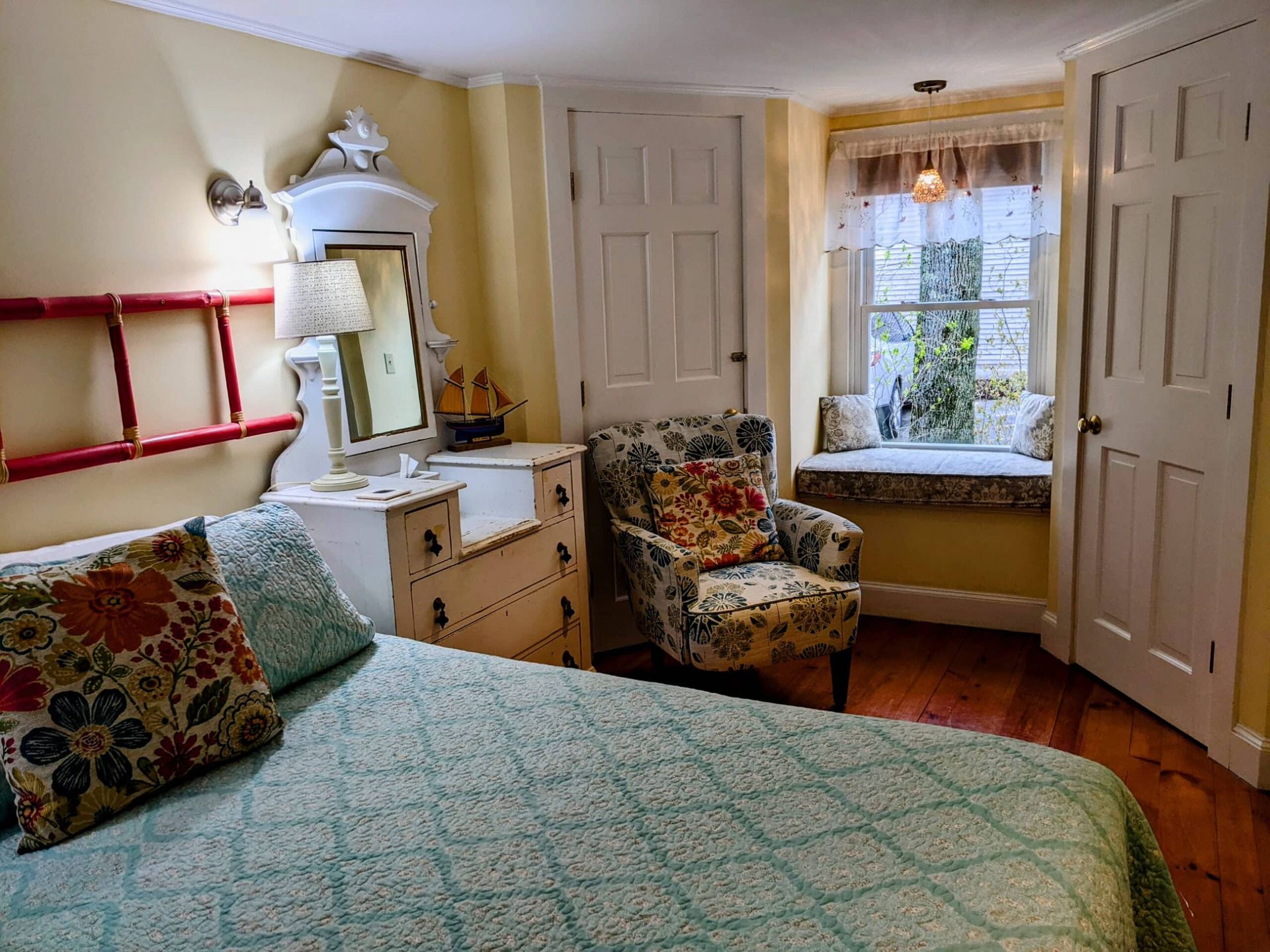 A bedroom with a bed , chair , dresser and window seat.