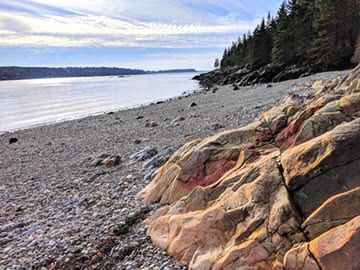 A rocky beach with a large rock in the foreground and a body of water in the background.