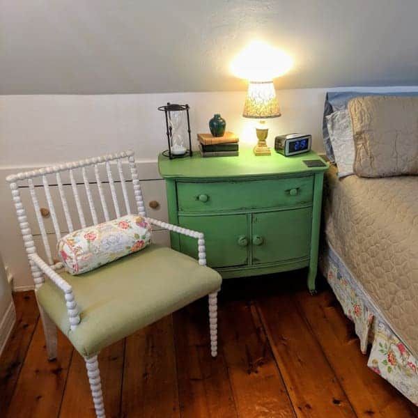 A bedroom with a green nightstand and a chair