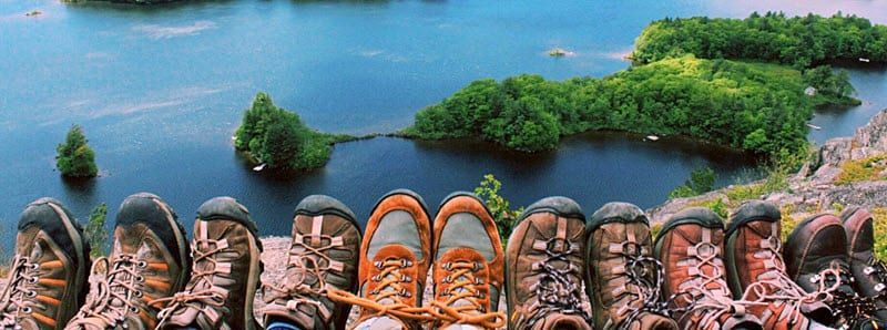 A row of hiking boots are lined up in front of a lake.