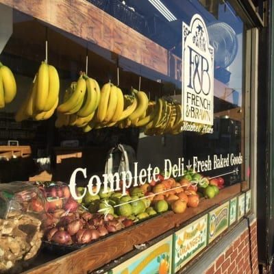 A display of fruits and vegetables in a window that says complete deli fresh baked goods