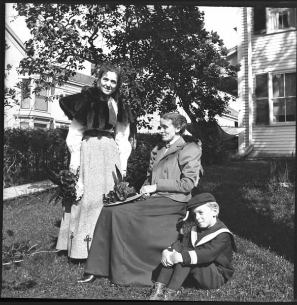 A black and white photo of three people in front of a house