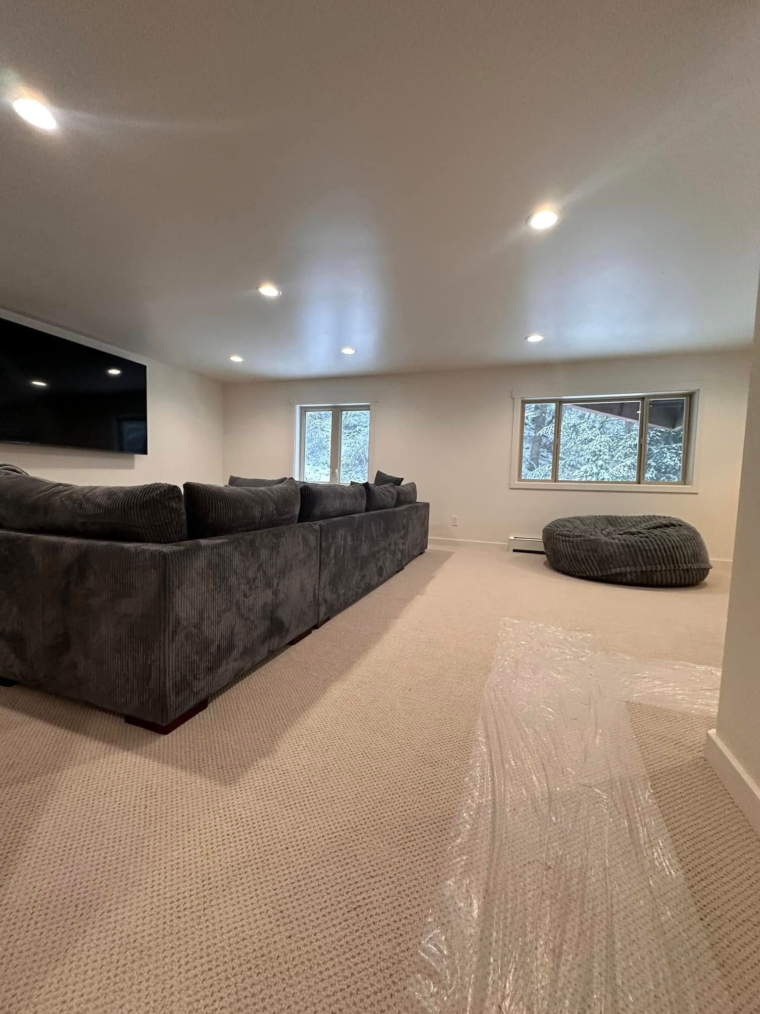 Large gray sectional sofa in a light room with a patterned carpet and two windows.