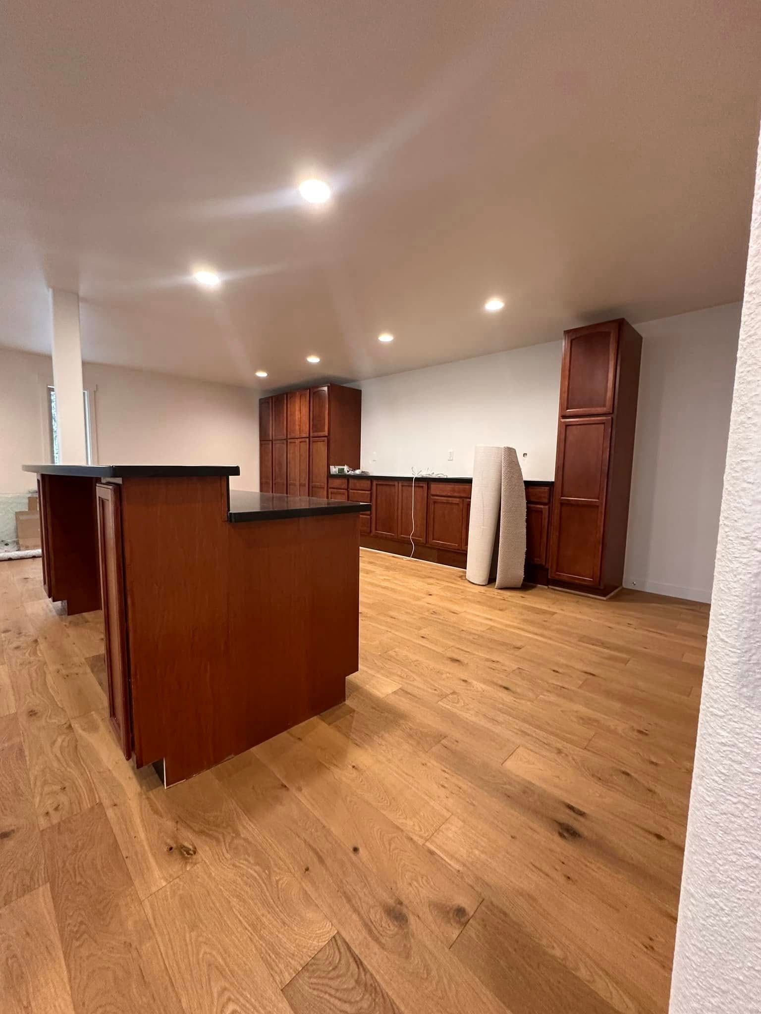 Empty kitchen with wood cabinets, black countertops, and wood floor; recessed lighting.