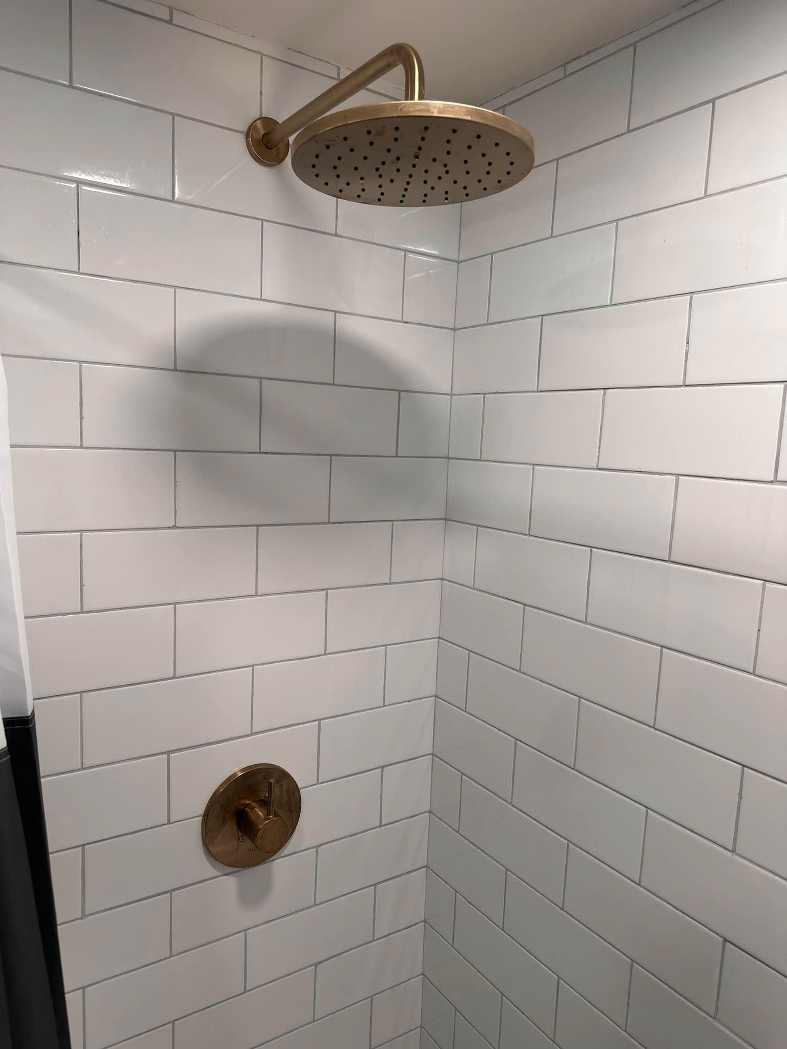 Gold shower head and faucet against white tiled wall.