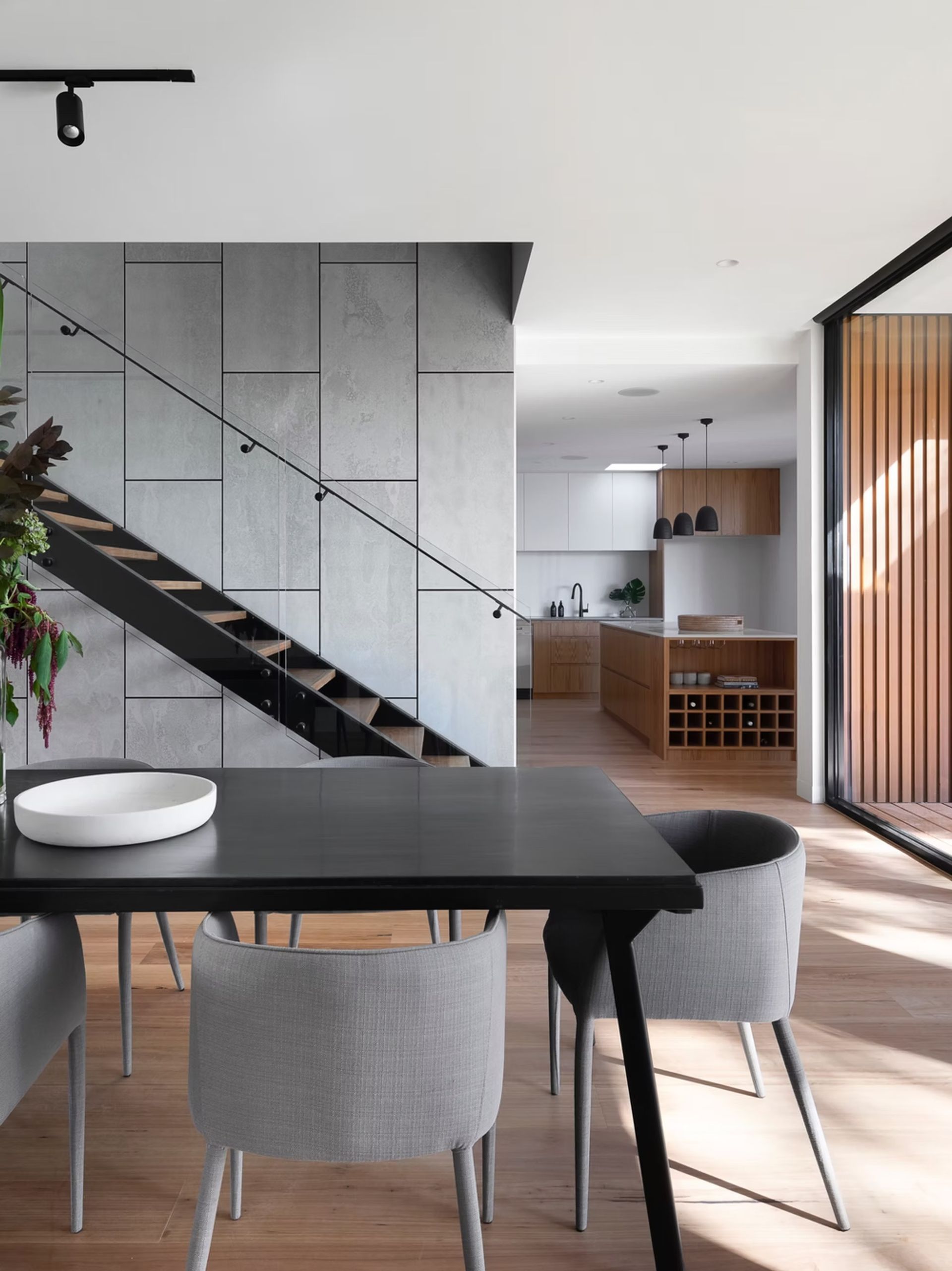 Dining area with dark table and gray chairs, next to a staircase with a concrete wall.