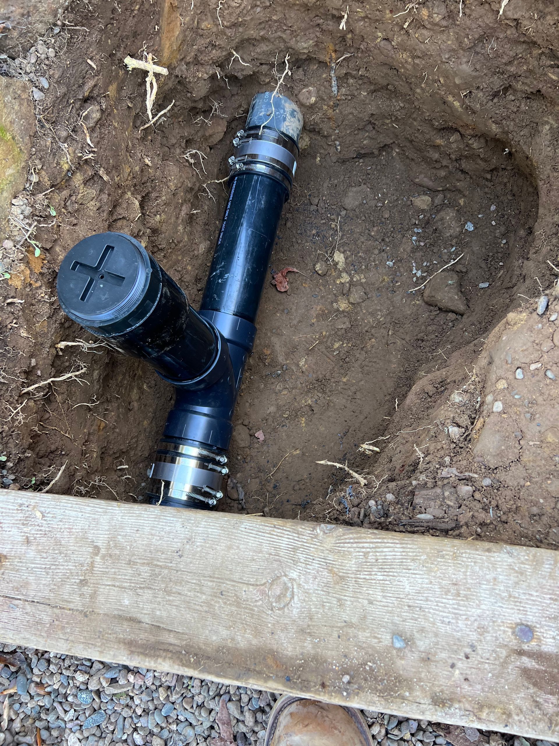 A Black Pipe Is Sitting In The Dirt Next To A Wooden Fence - Oxnard, CA - 4J's Plumbing And Drain Cleaning