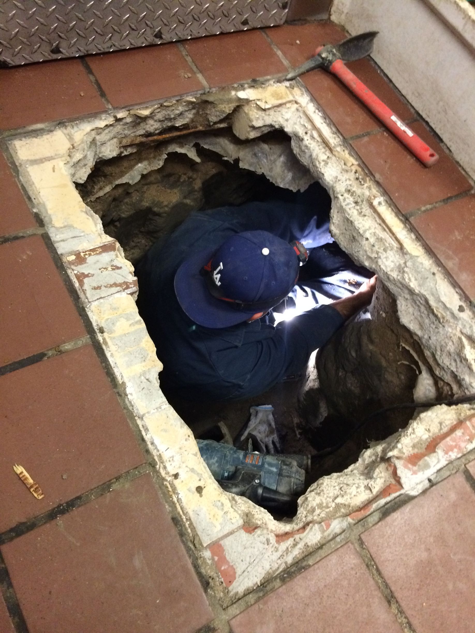 A Man In A Blue Hat Is Working In A Hole In The Floor - Oxnard, CA – 4J's Plumbing And Drain Cleaning