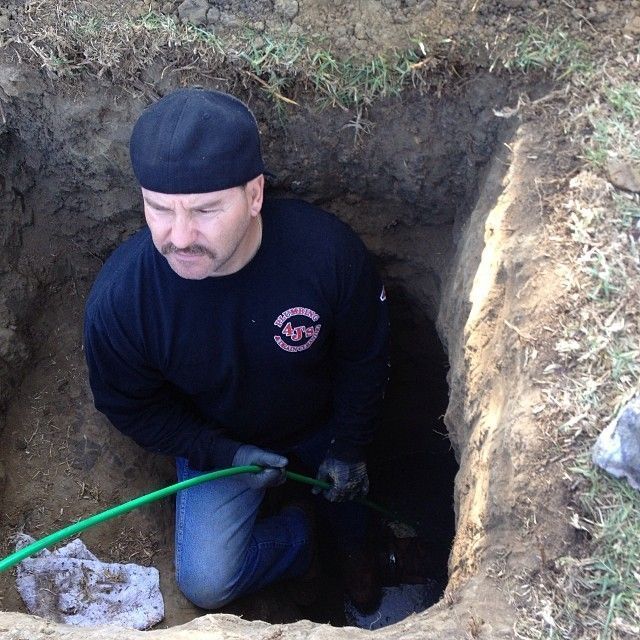A Man Is Kneeling In A Hole Holding A Green Hose - Oxnard, CA – 4J's Plumbing And Drain Cleaning