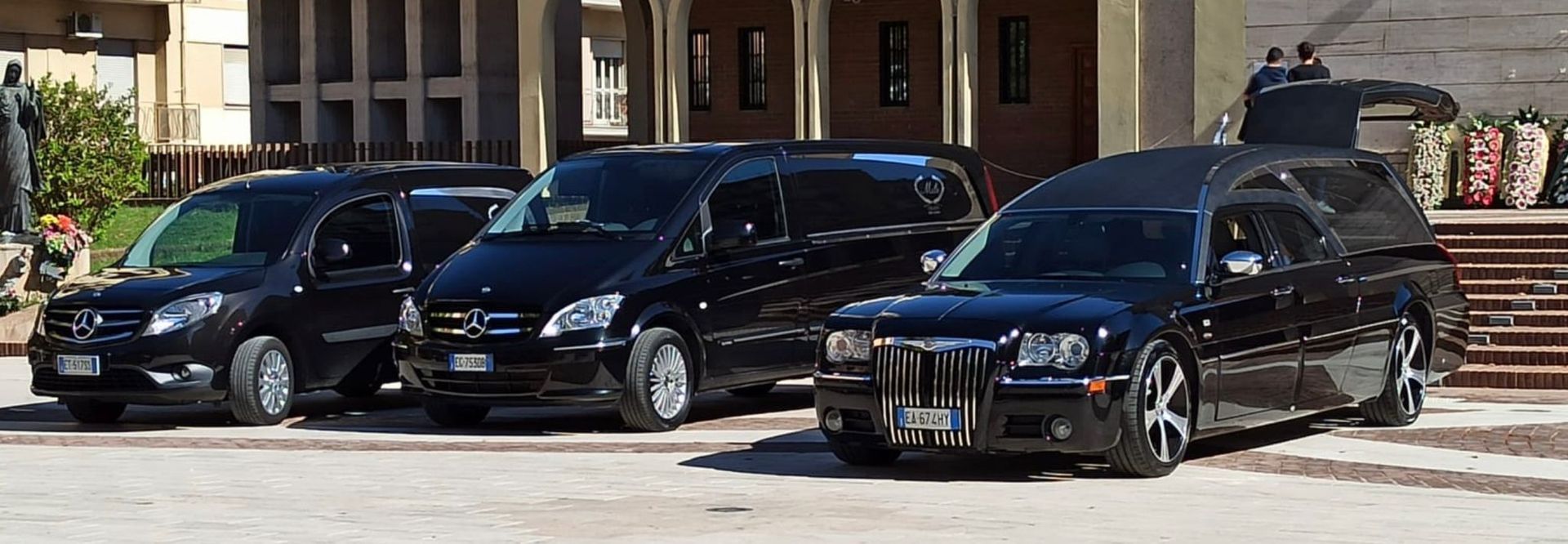 Una fila di auto nere sono parcheggiate davanti a un edificio.