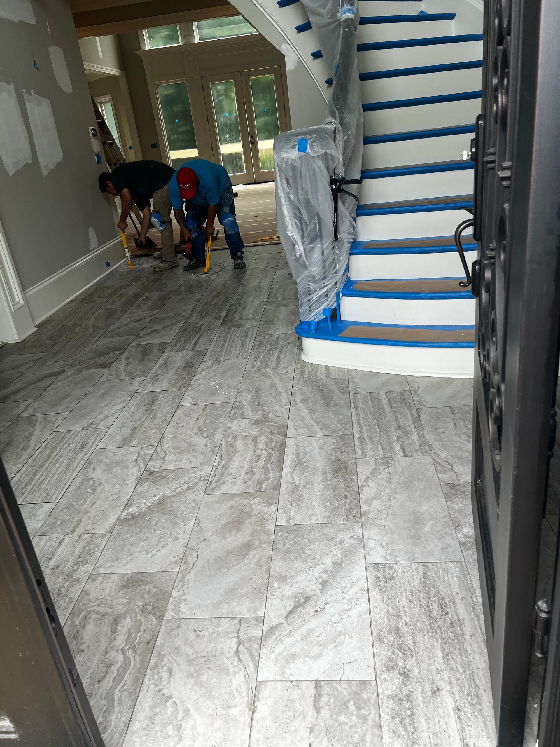 A man is working on a tile floor in a room next to a staircase.