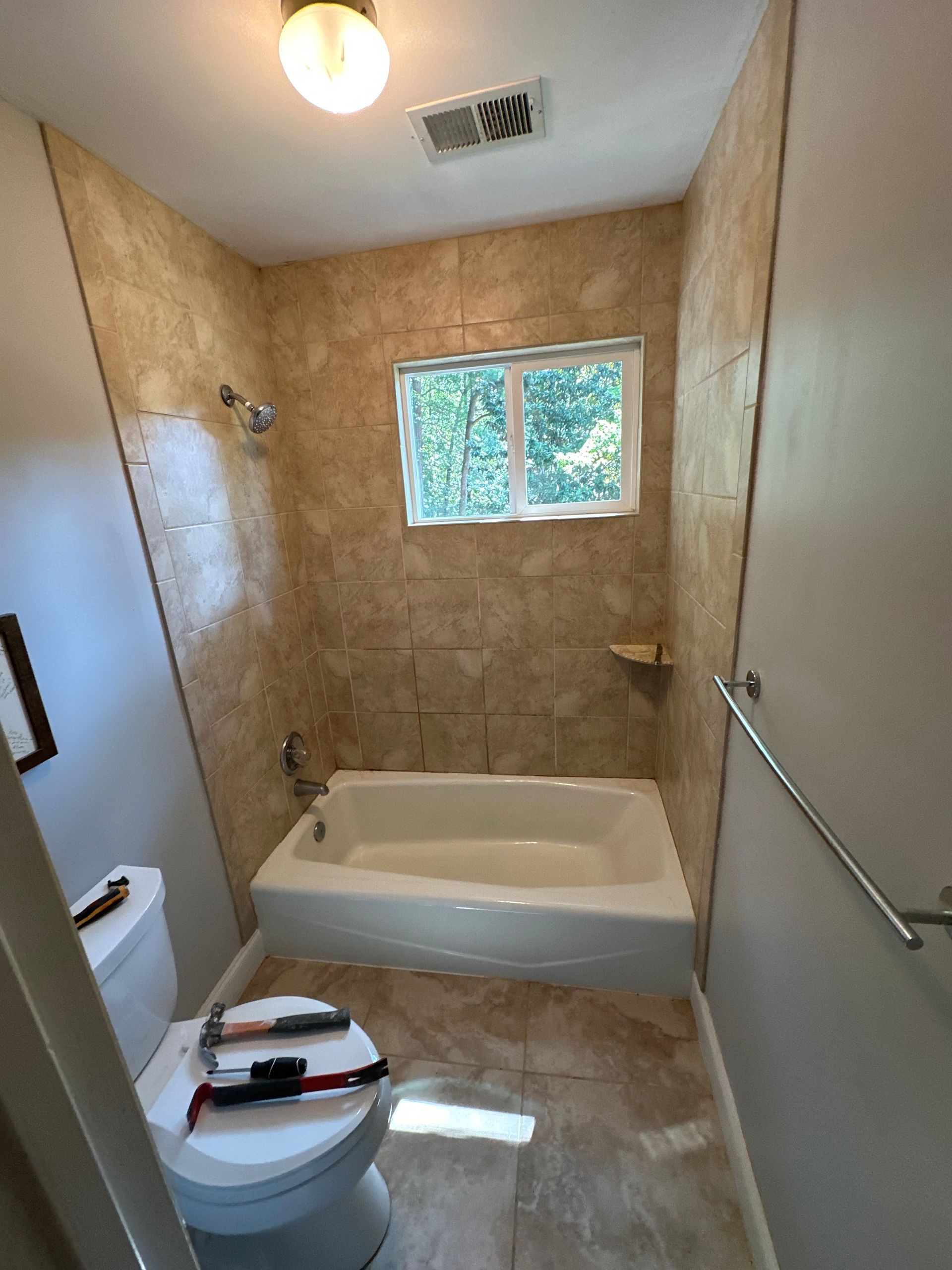 A bathroom with a toilet , bathtub and window.