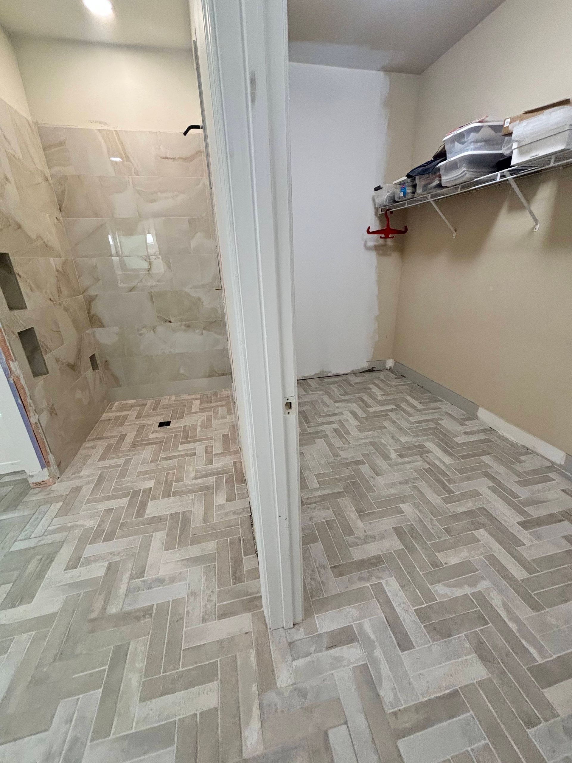 A walk in closet with a walk in shower and a herringbone floor.