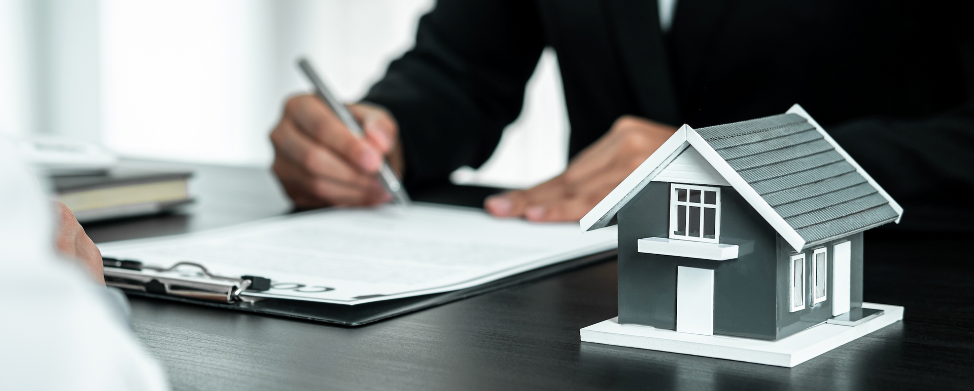 A man is signing a document next to a model house.