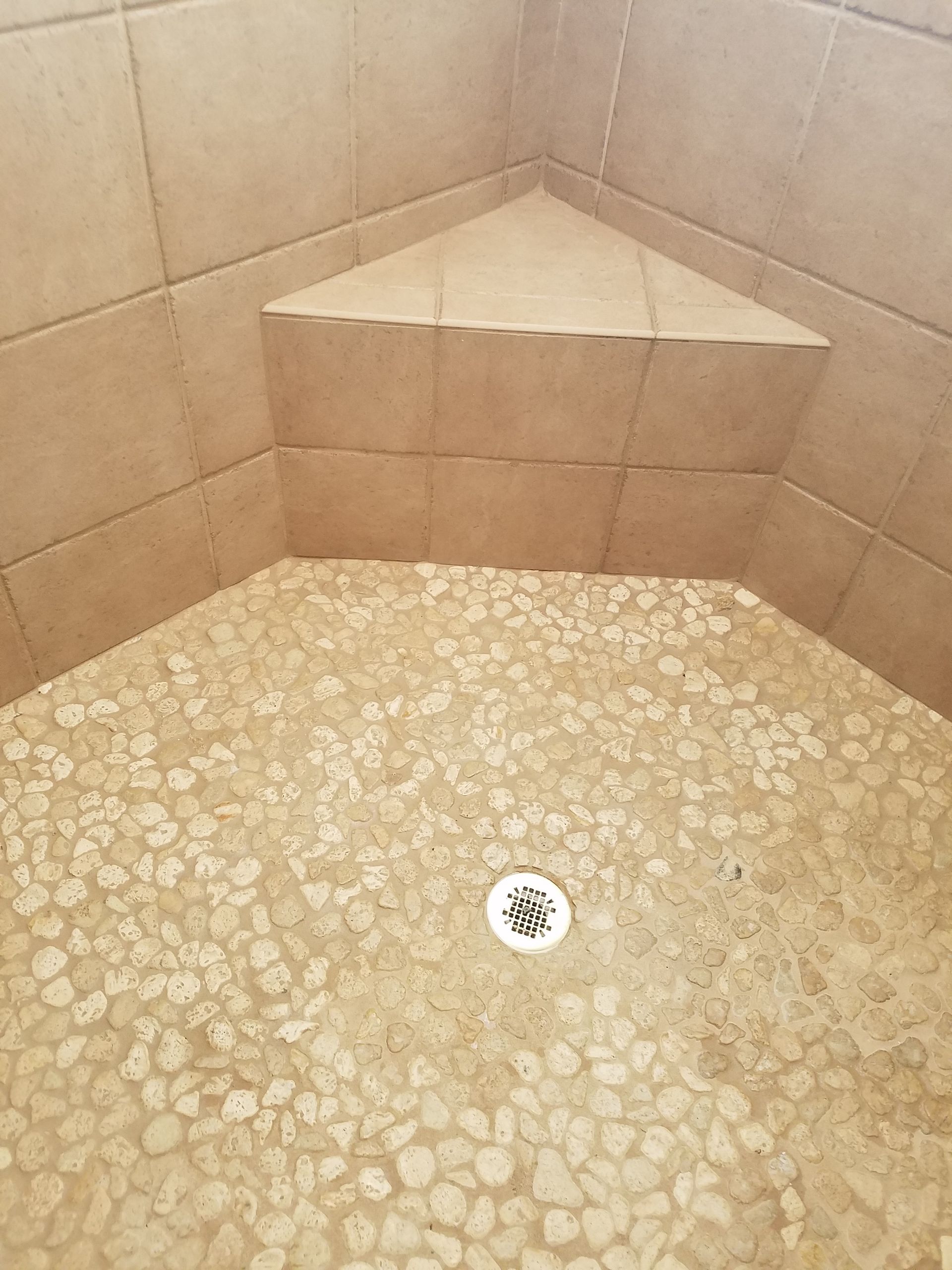A shower stall with a corner seat and a drain.