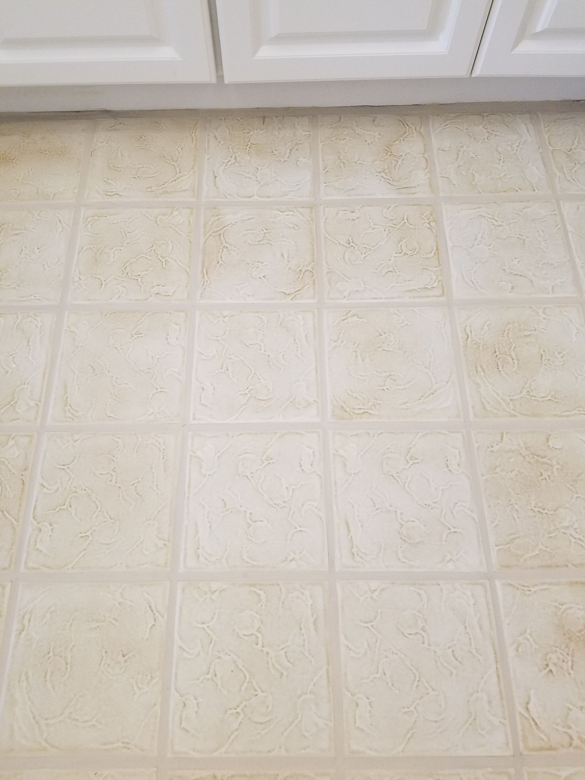 A close up of a tiled floor in a kitchen with white cabinets.