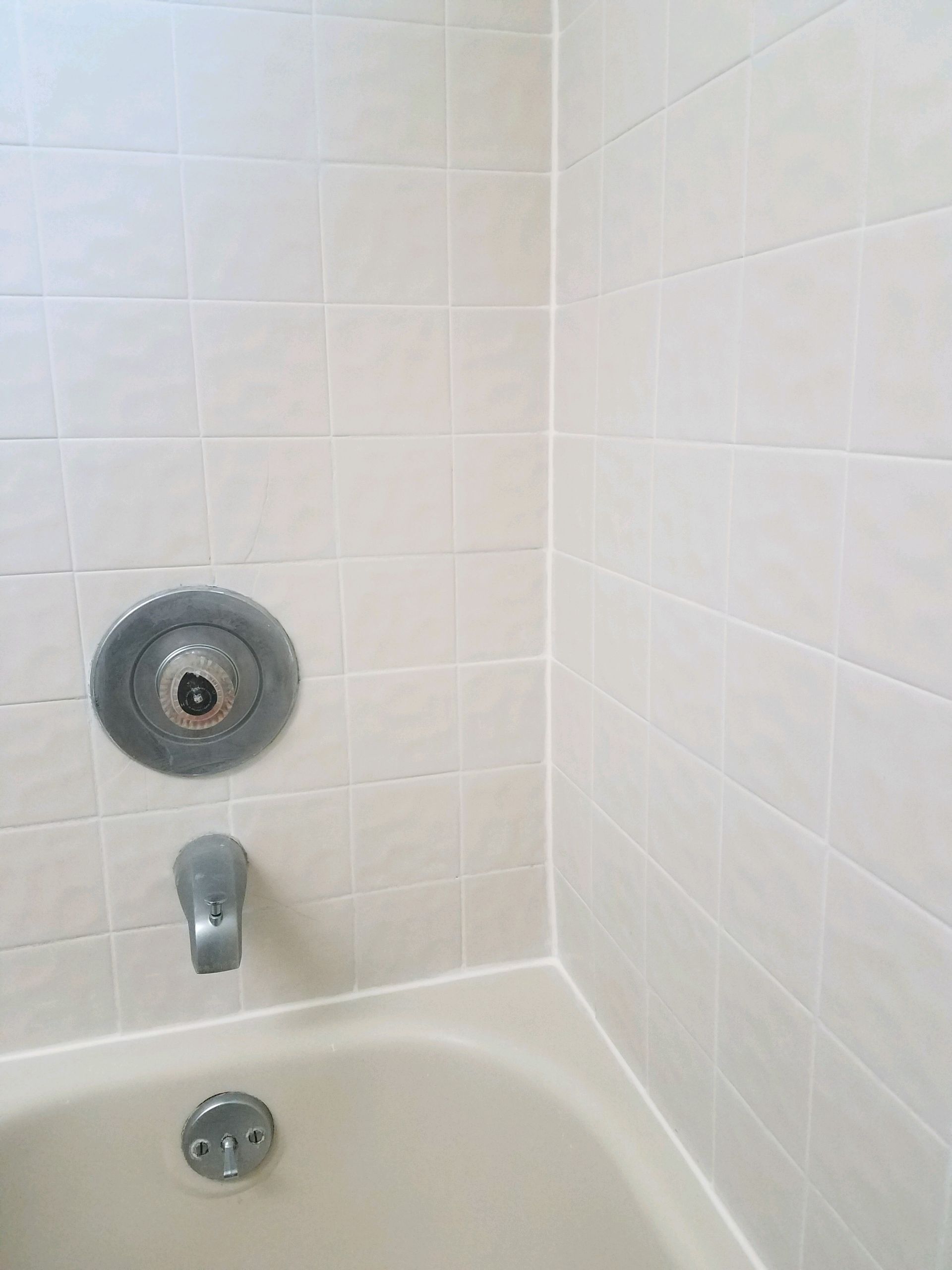 A bathtub in a bathroom with white tiles and a shower head.
