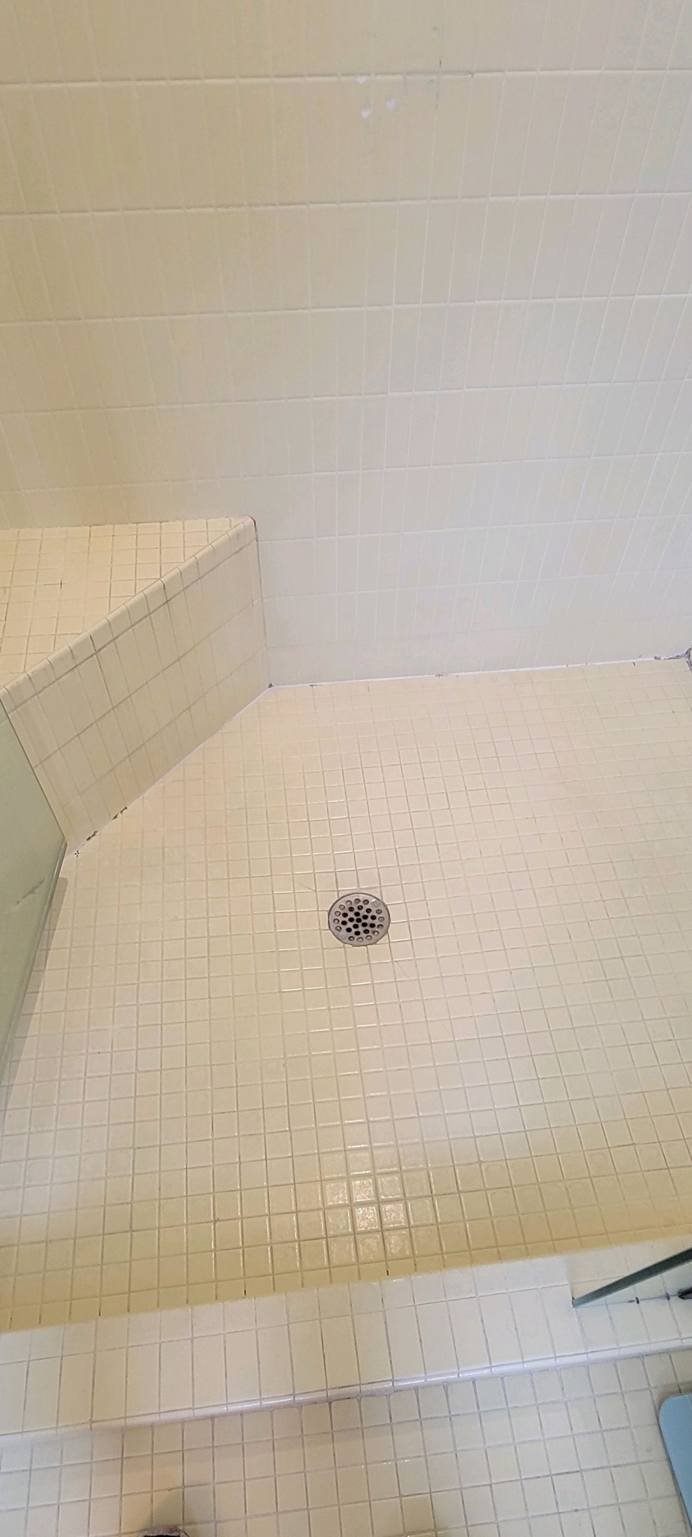 A bathroom with white tiles and a shower stall with a drain.