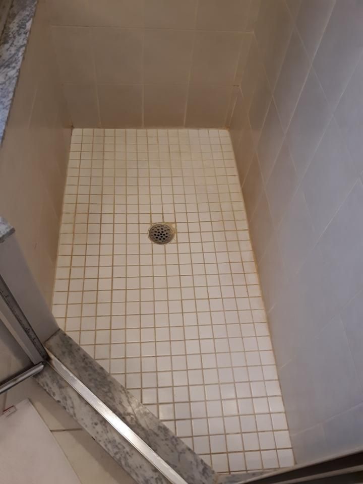 A shower stall with white tiles and a drain.