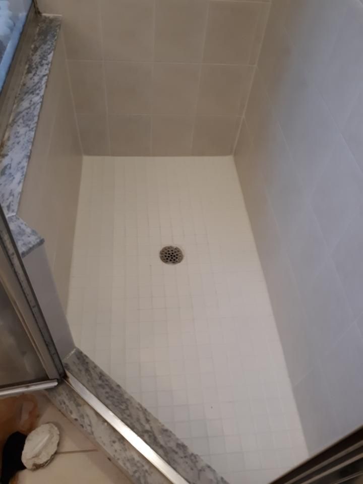 A shower stall with a drain on the floor in a bathroom.
