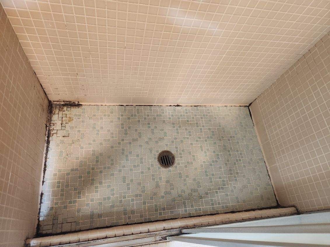 A dirty shower stall with a drain in the middle of it.