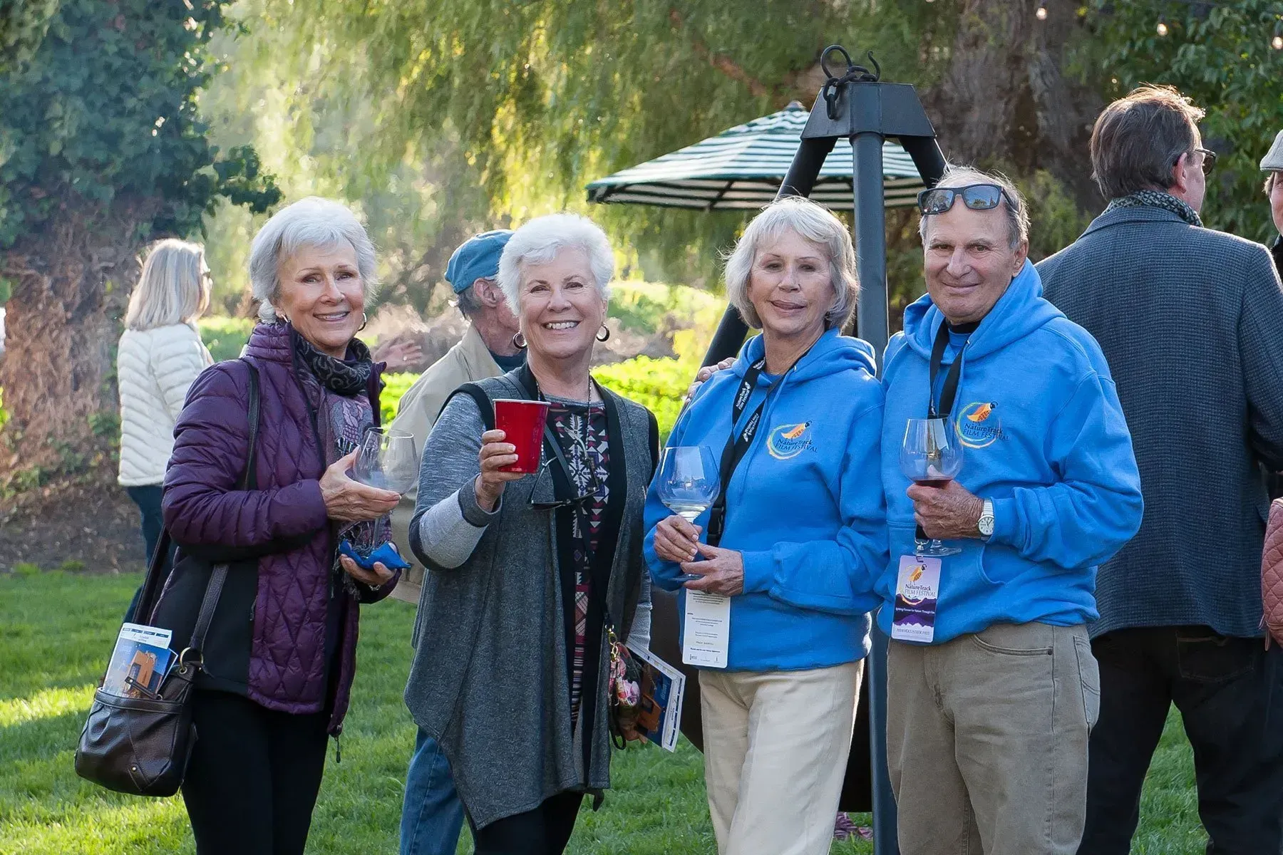 A group of people are standing in the grass holding wine glasses.