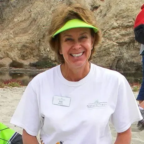 A woman wearing a white shirt and a green visor is smiling.