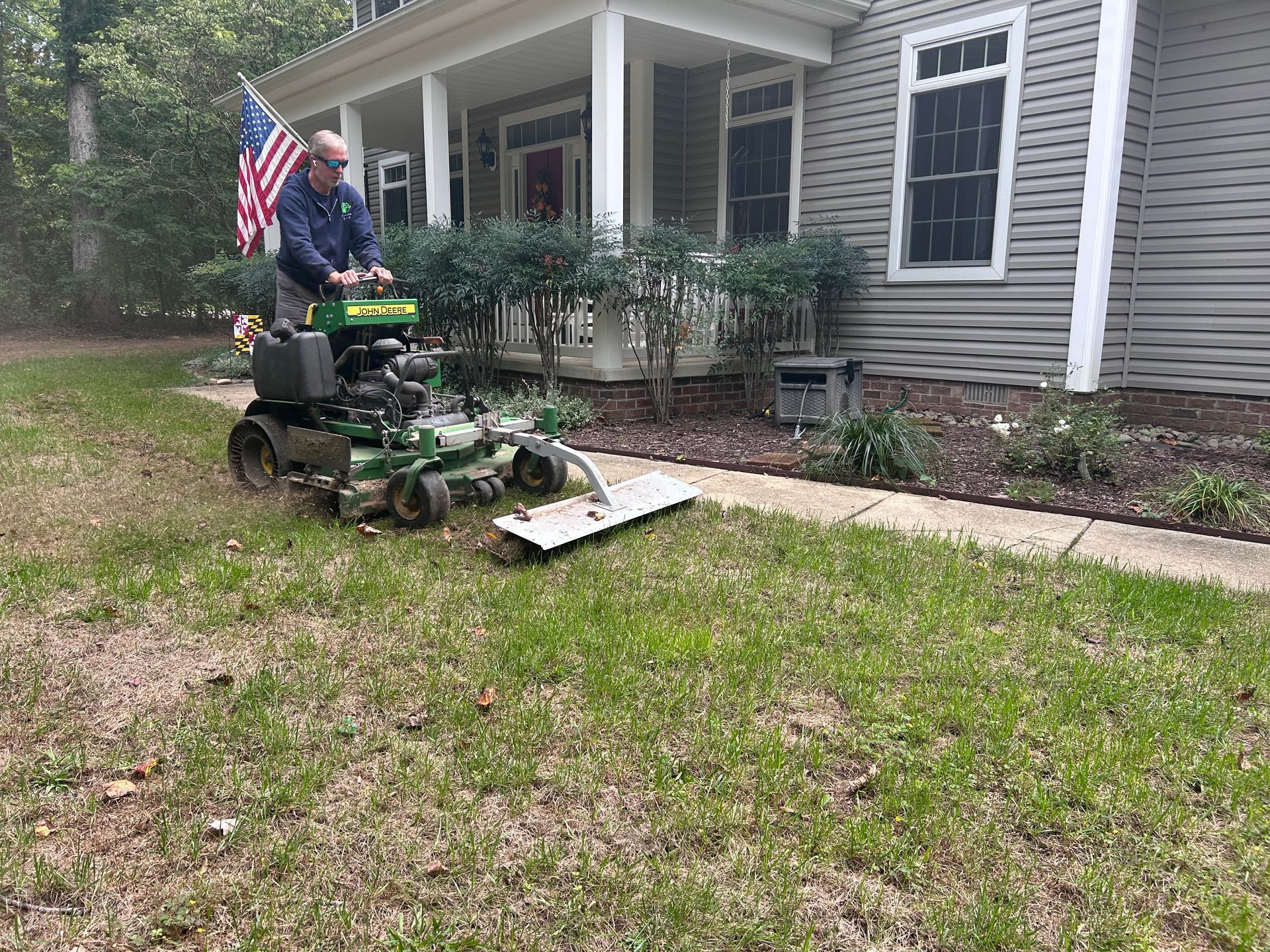 Man mowing lawn with a green machine beside a house with an American flag.
