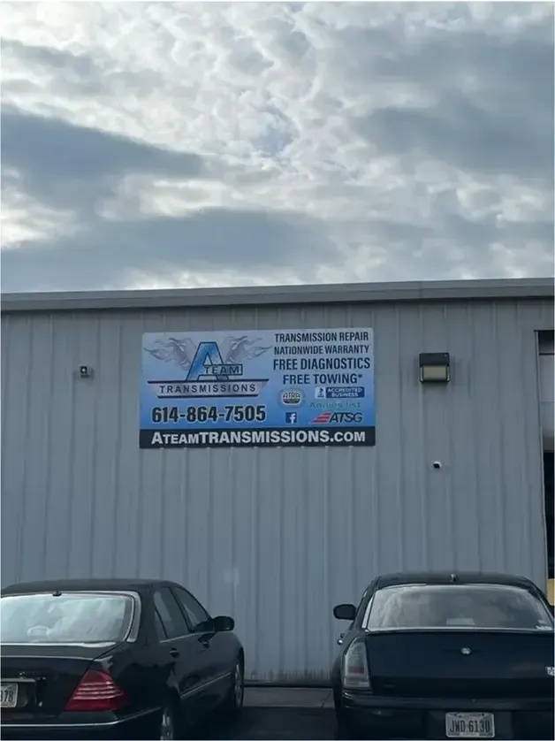 Two lifted off-road jeeps parked outside an auto shop under a tall billboard sign.