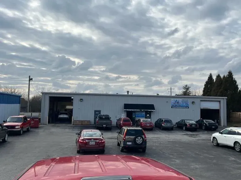 Beige auto repair shop with open garage bays and a blue trash bin outside.