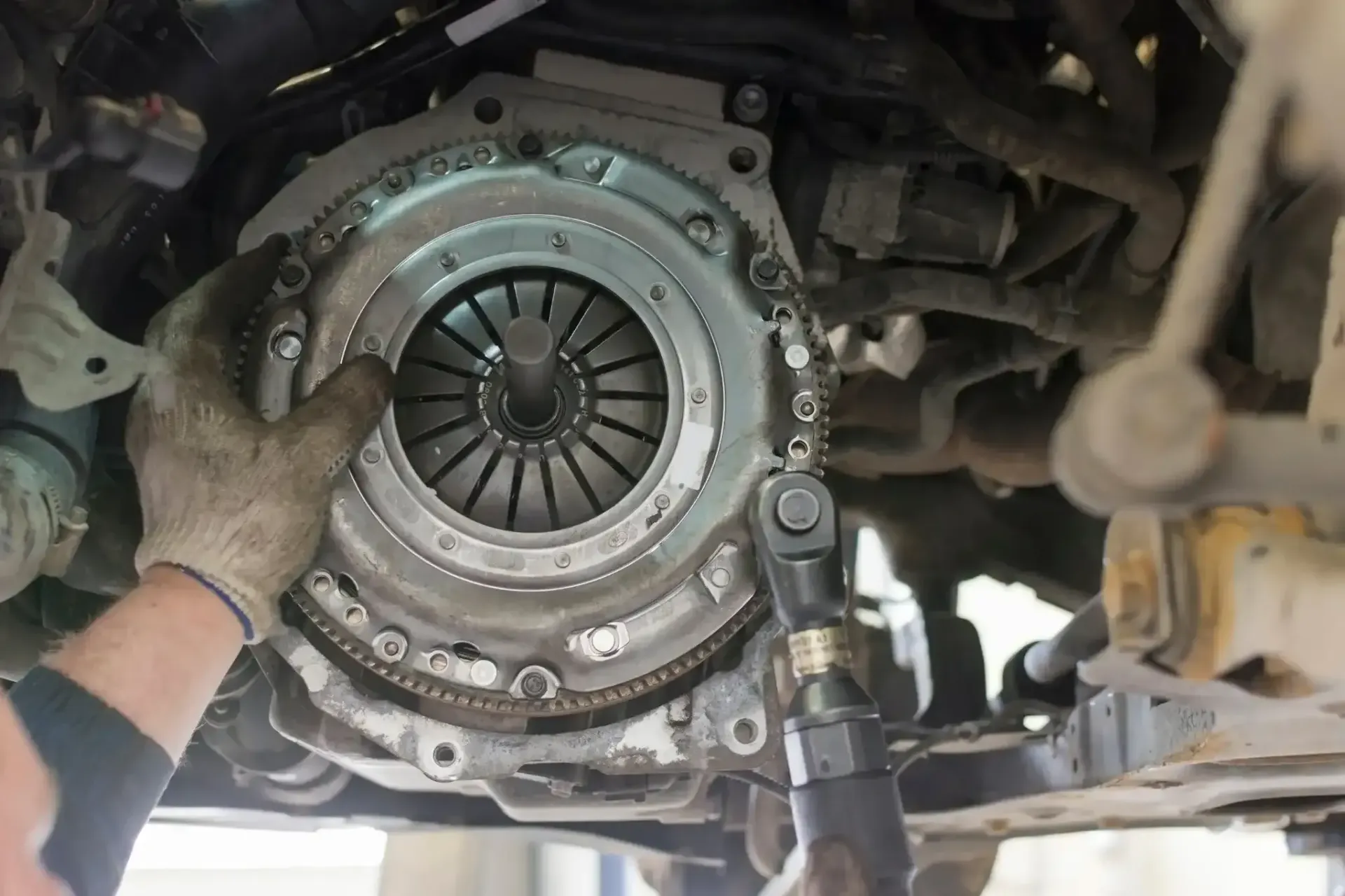 Mechanic replacing a clutch on a vehicle, with gloved hands and tools undercarriage visible