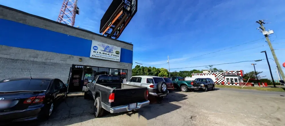 Street view of a blue storefront with parked vehicles and a pickup truck under a bright sky