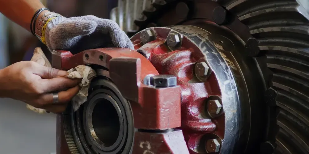 Hands working on a red mechanical bearing or gear assembly with tools
