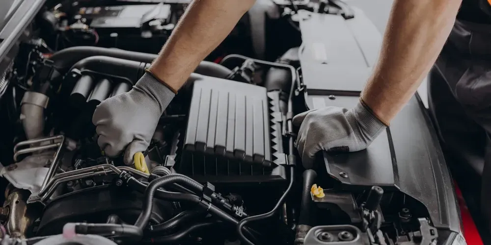 Gloved hands working on a car engine in a garage, with black engine components visible.