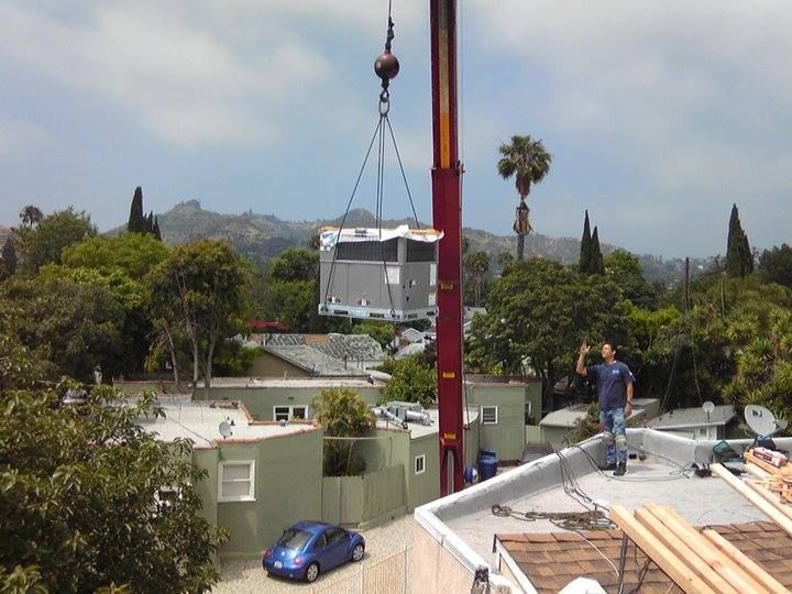 A man is standing on a roof while a crane lifts a building