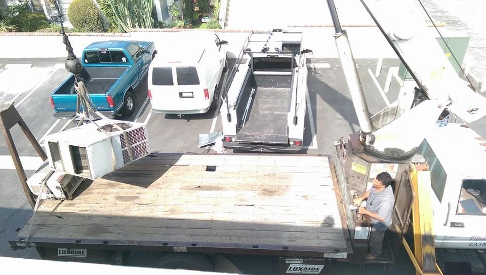 A tow truck is being lifted by a crane in a parking lot