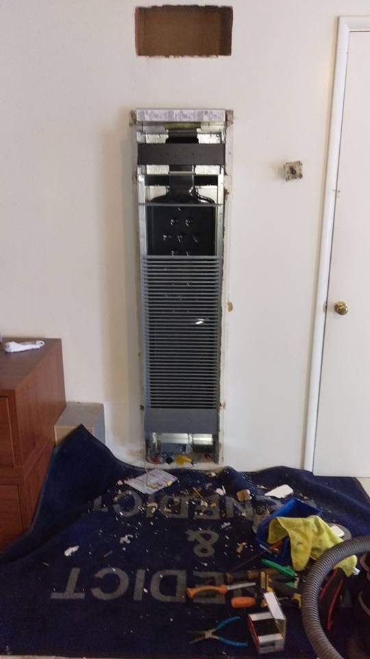 A refrigerator is being repaired in a living room.