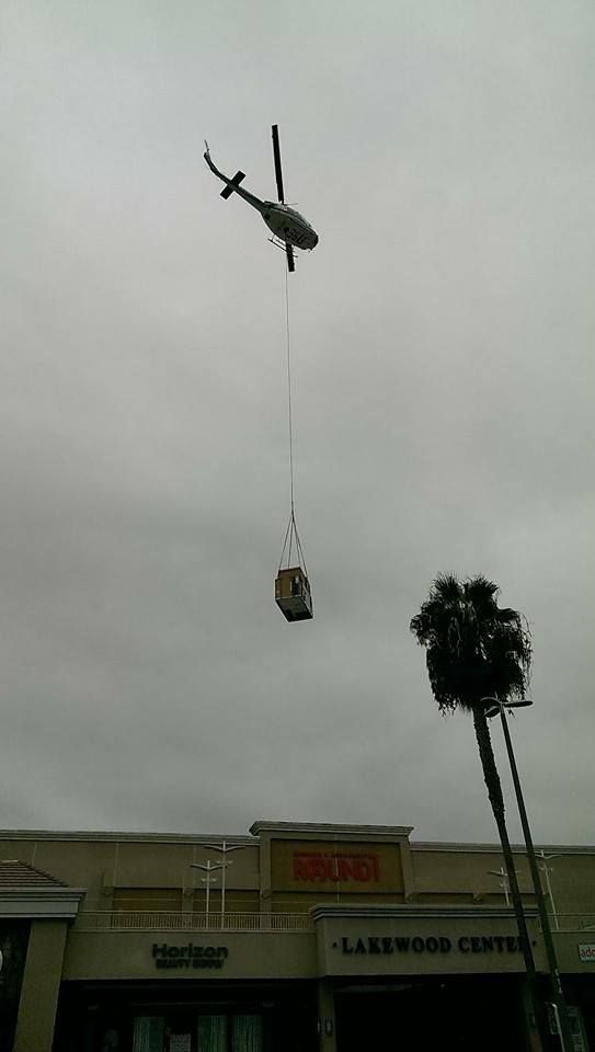 A helicopter is lifting a box in the air over a building.