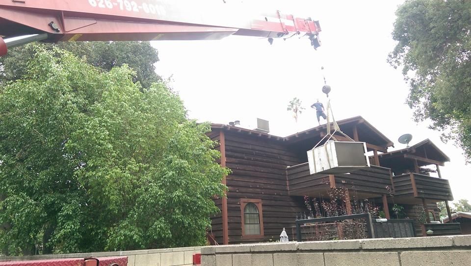 A red crane is lifting a large item from the roof of a house.