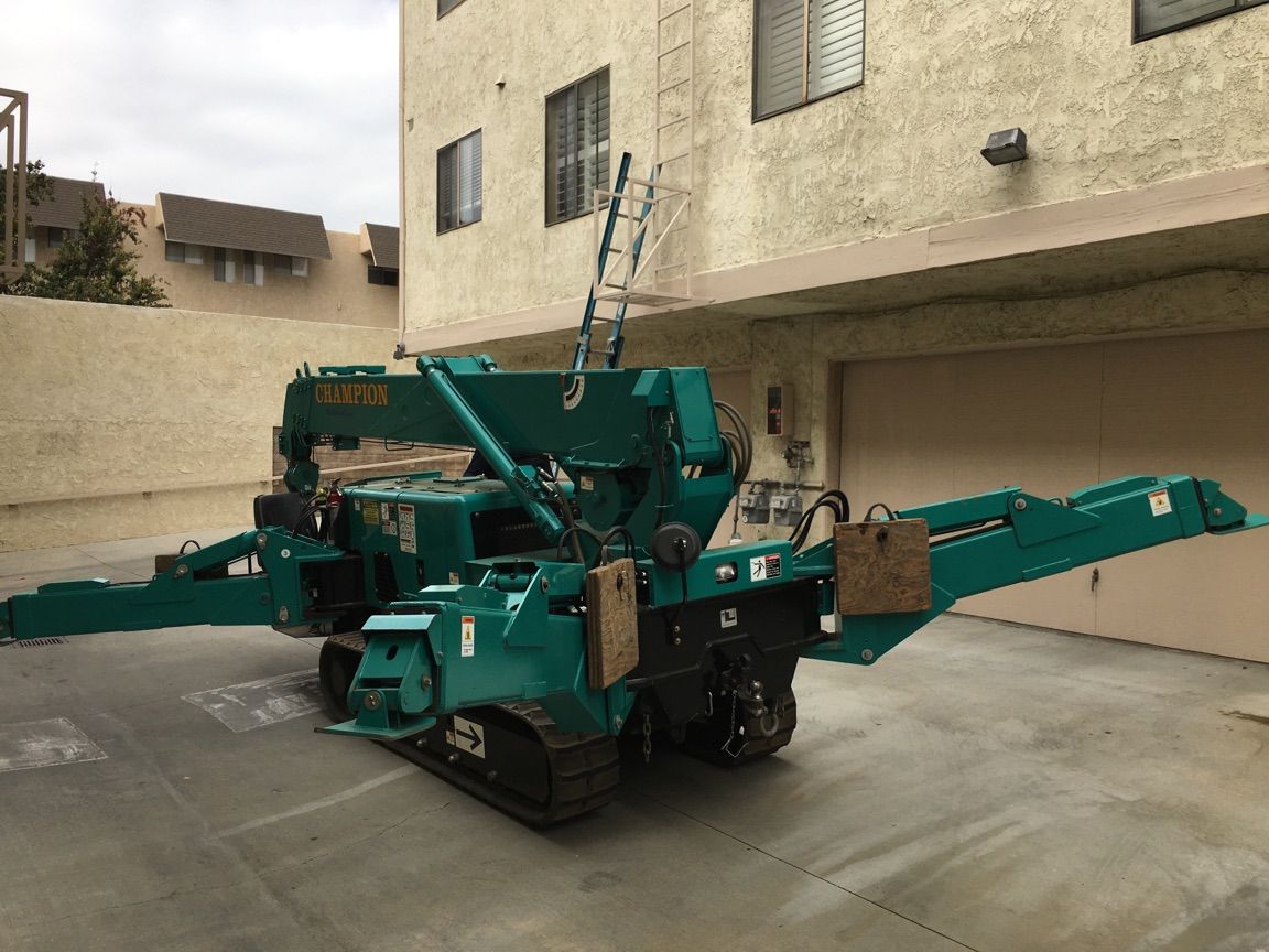 A green crane is parked in a parking lot in front of a building.