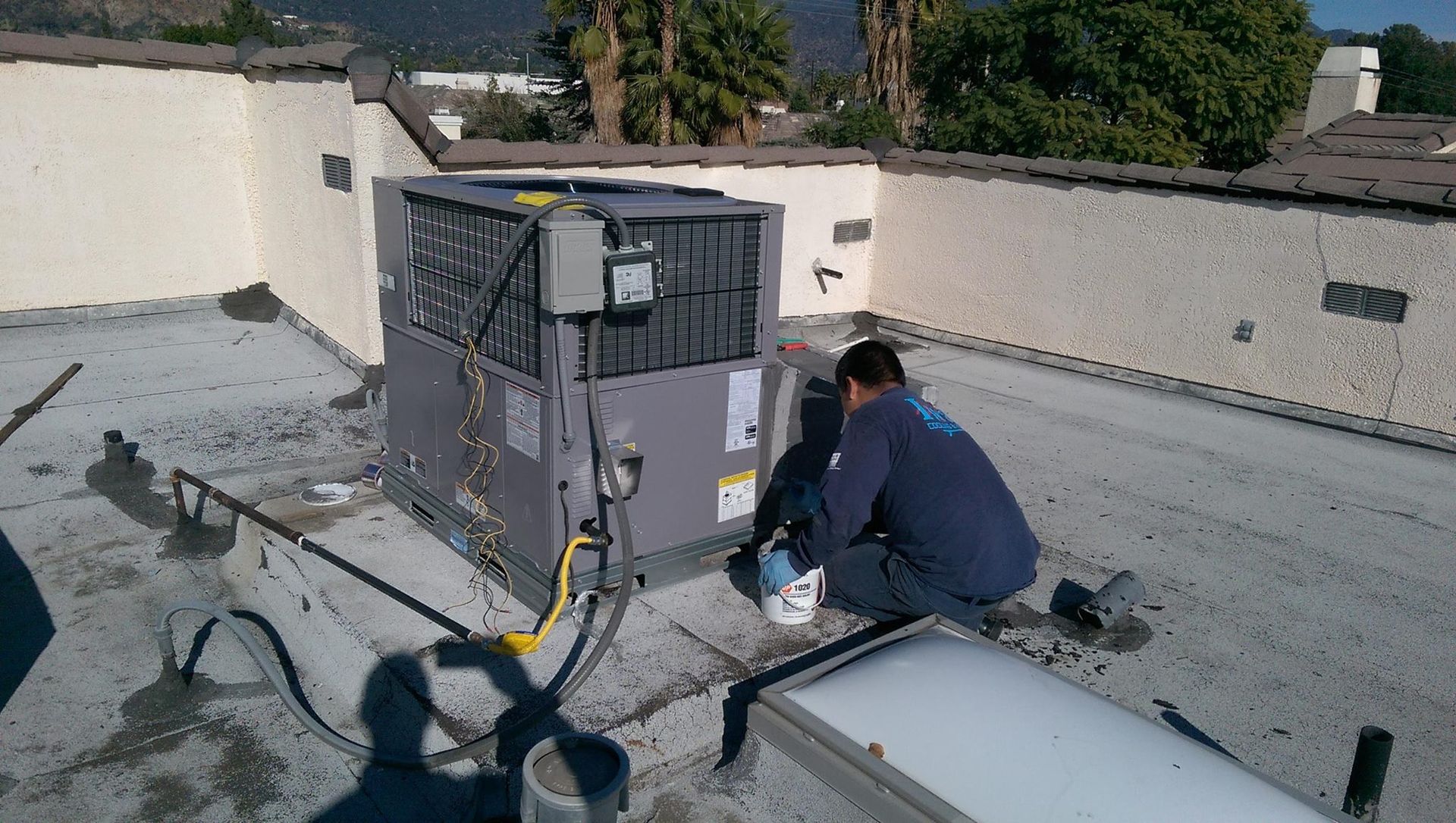 A man is working on an air conditioner on the roof of a building.