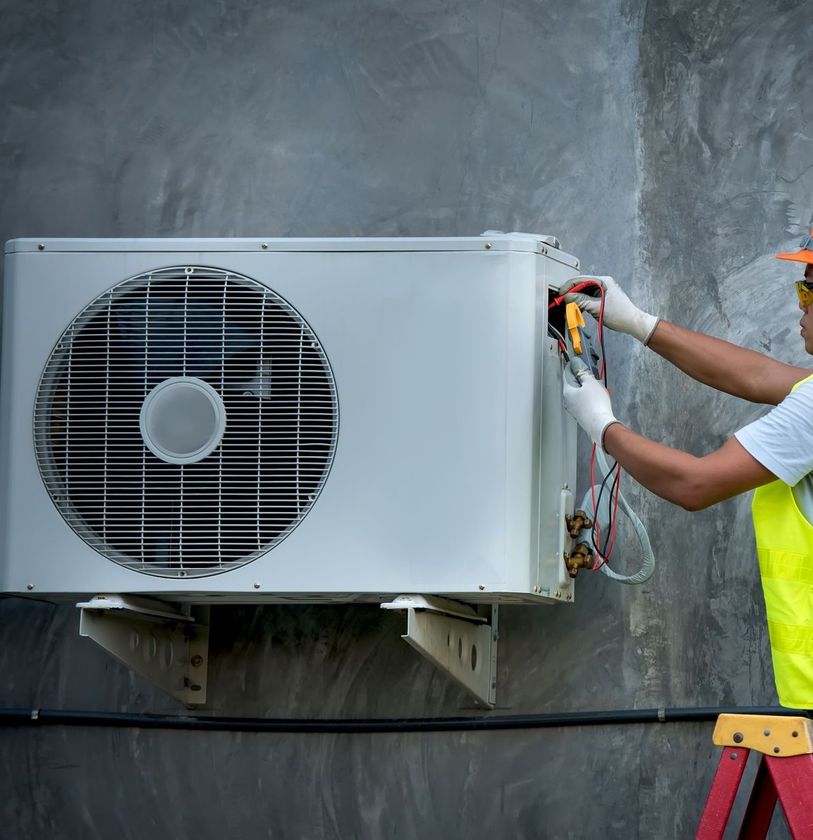 A man is standing on a ladder fixing an air conditioner.