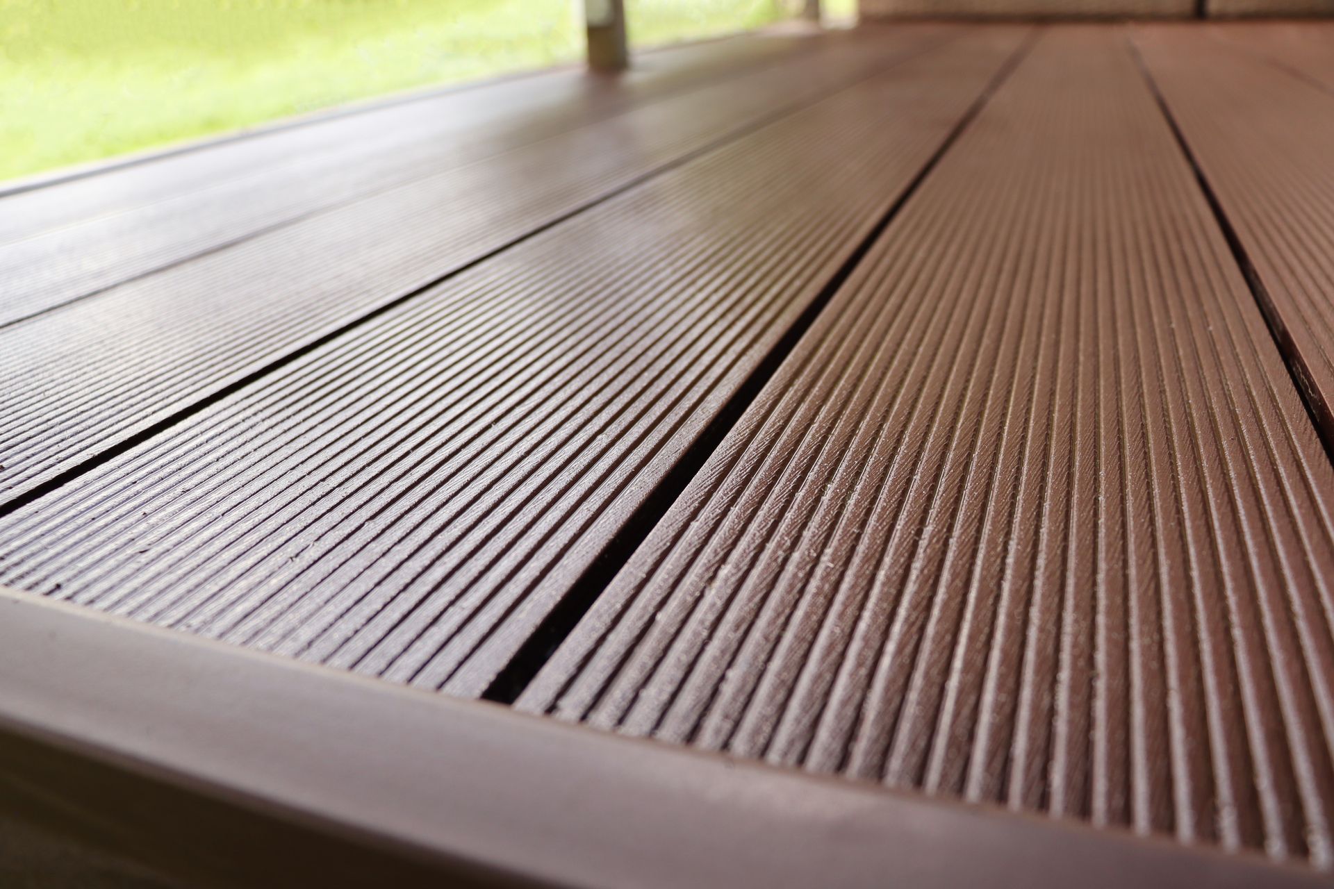 Gros plan sur des lames de terrasse composites brunes et nervurées, posées en lignes parallèles sur une terrasse extérieure.