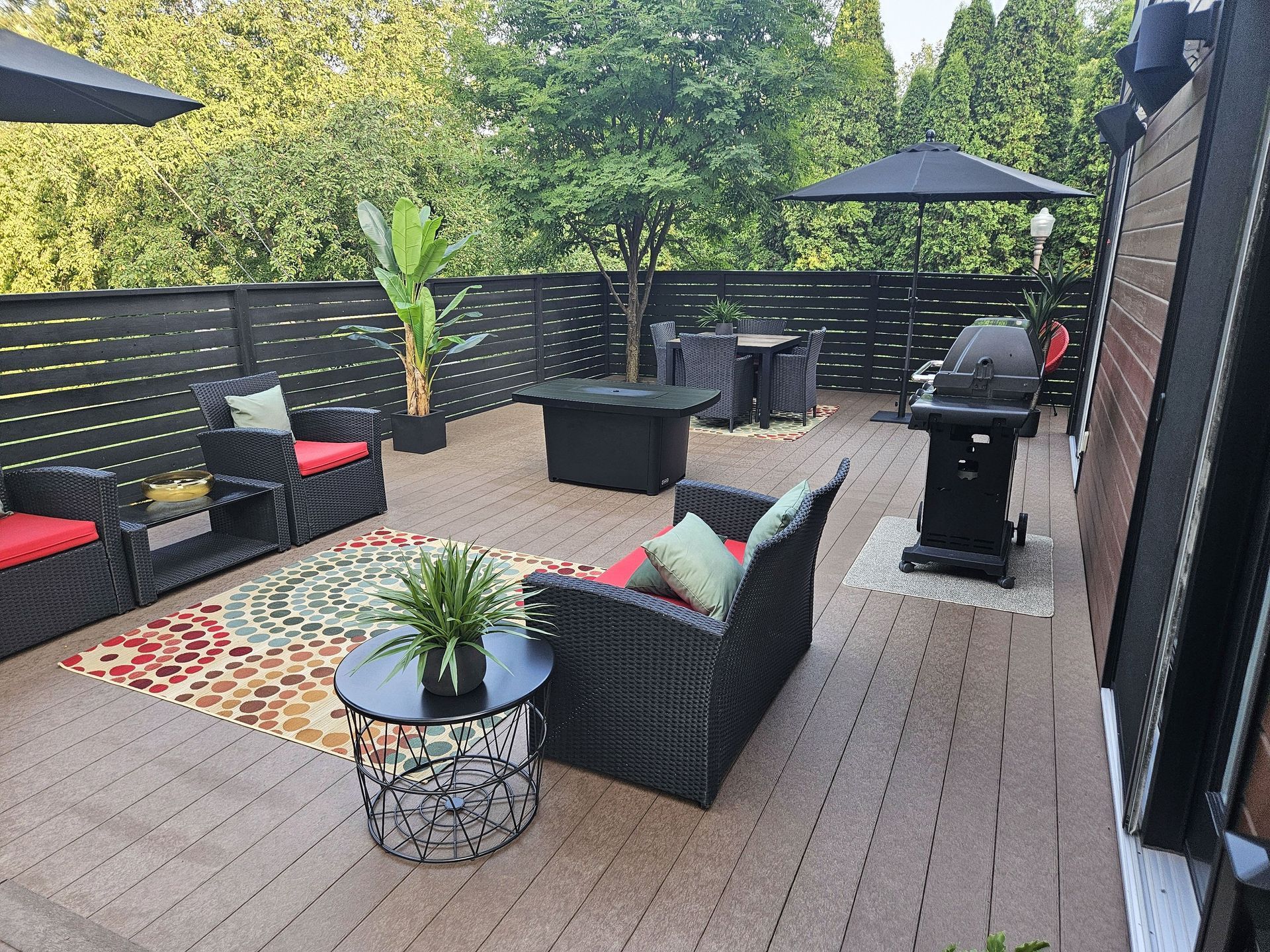 Une terrasse sur le toit avec des meubles en osier, un tapis coloré, un foyer, un barbecue et des plantes en pot, le tout adossé à une clôture en bois.